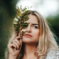 Vibrant woman holding a fern leaf outdoors, showcasing natural beauty and skincare, emphasizing organic and eco-friendly dermatological treatments offered by Shrinika Derma Care.